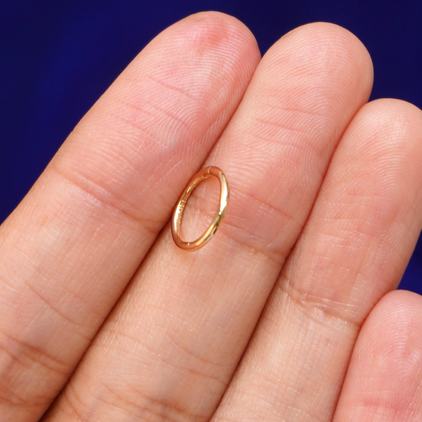 A model holding a Small Seamless Huggie sideways between two fingers to show the thickness of the hoop