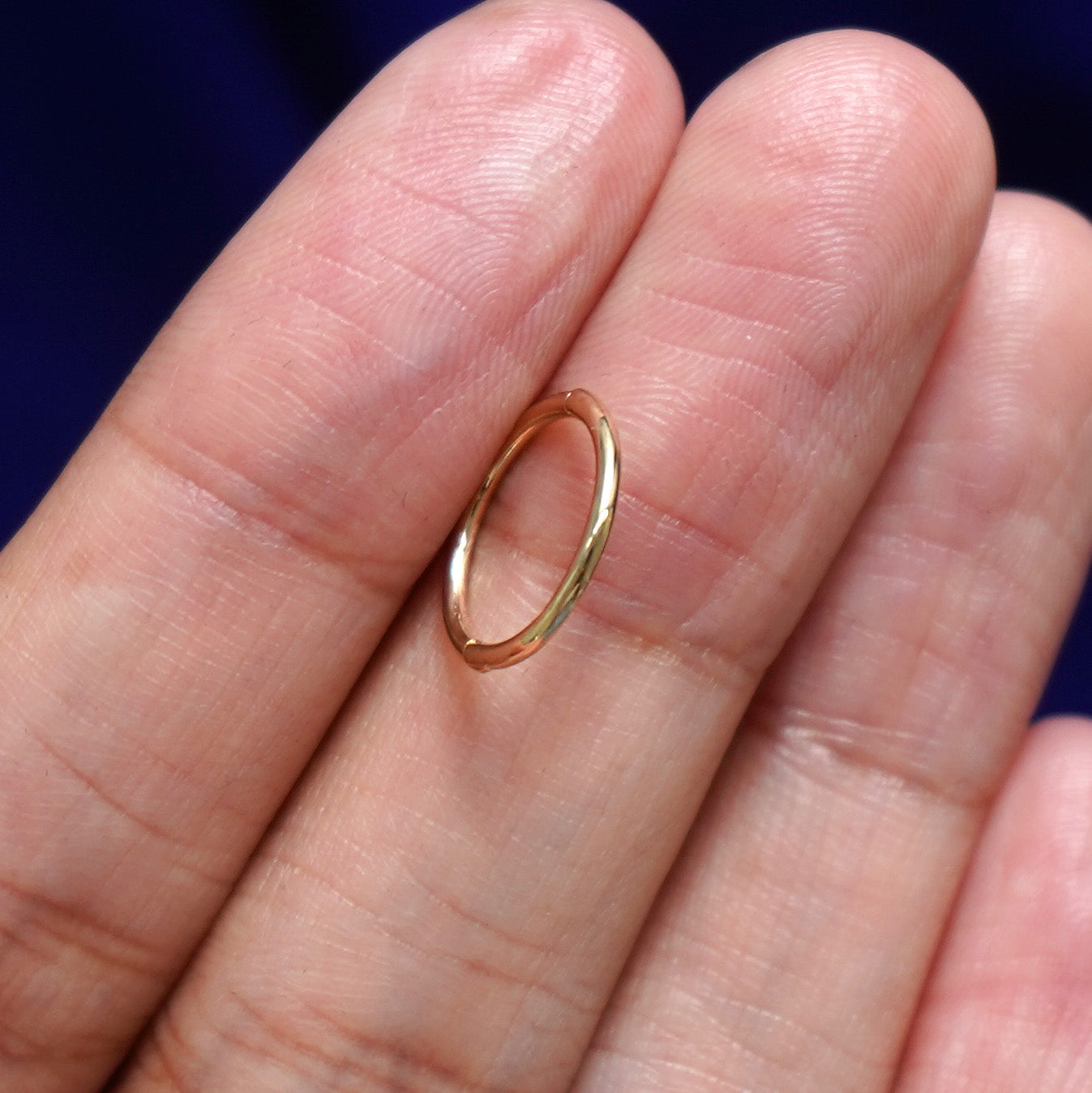 A model holding a Medium Seamless Huggie sideways between two fingers to show the thickness of the hoop