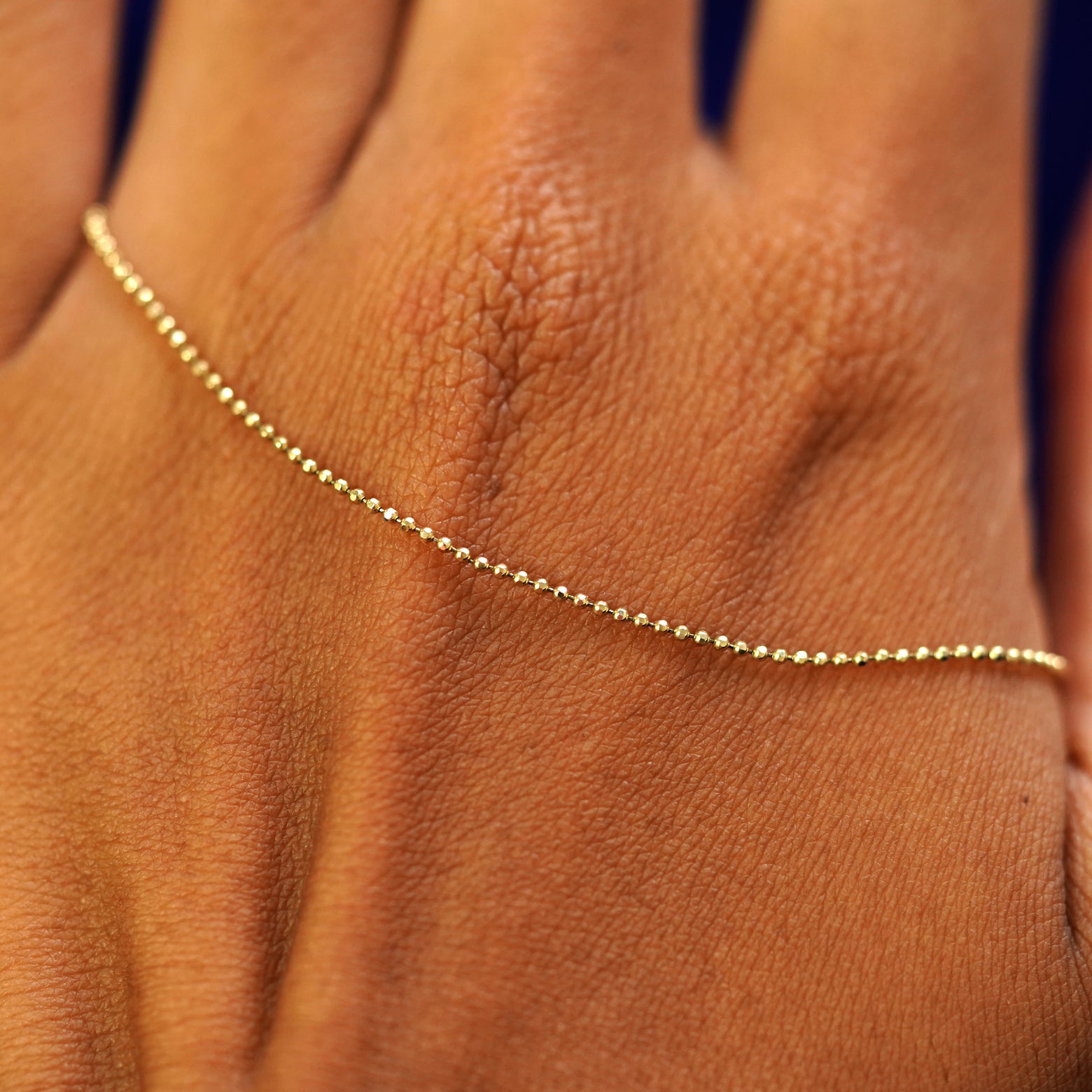 A solid gold Bead Necklace resting on the back of a model's hand