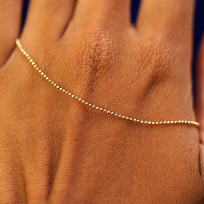 A solid gold Bead Necklace resting on the back of a model's hand