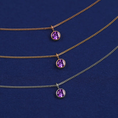 Three versions of the Amethyst Necklace shown in options of yellow, white and rose gold on a dark blue background