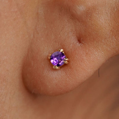 Close up view of a model's ear wearing a 14k yellow gold Amethyst Studd Earring