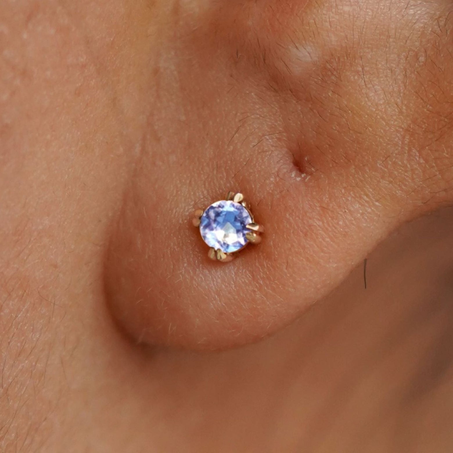 Close up view of a model's ear wearing a 14k yellow gold Aquamarine Stud Earring