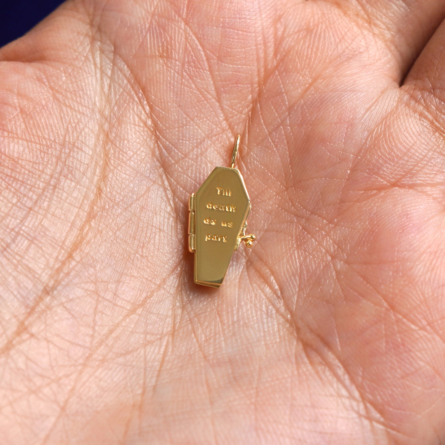 A closed solid gold Coffin Charm for chain resting in a model's palm