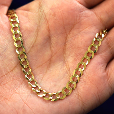 A yellow gold Curb Bracelet draped on a model's palm