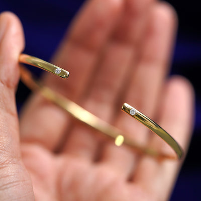 A yellow gold Diamond Open Bangle Bracelet resting between a model's fingers