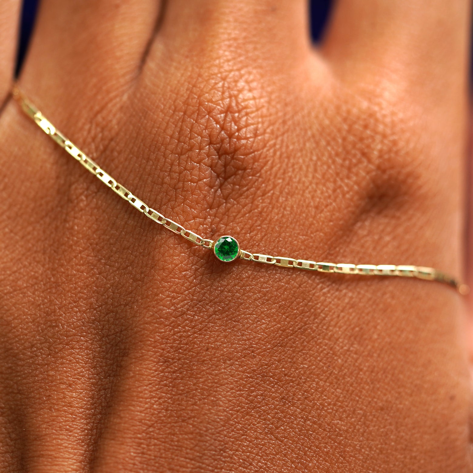 A solid gold Emerald Bracelet resting on the back of a model's hand