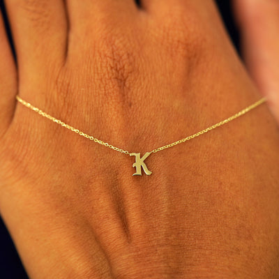 A solid 14k gold Initial Necklace with the letter K draped across the back of a model's hand