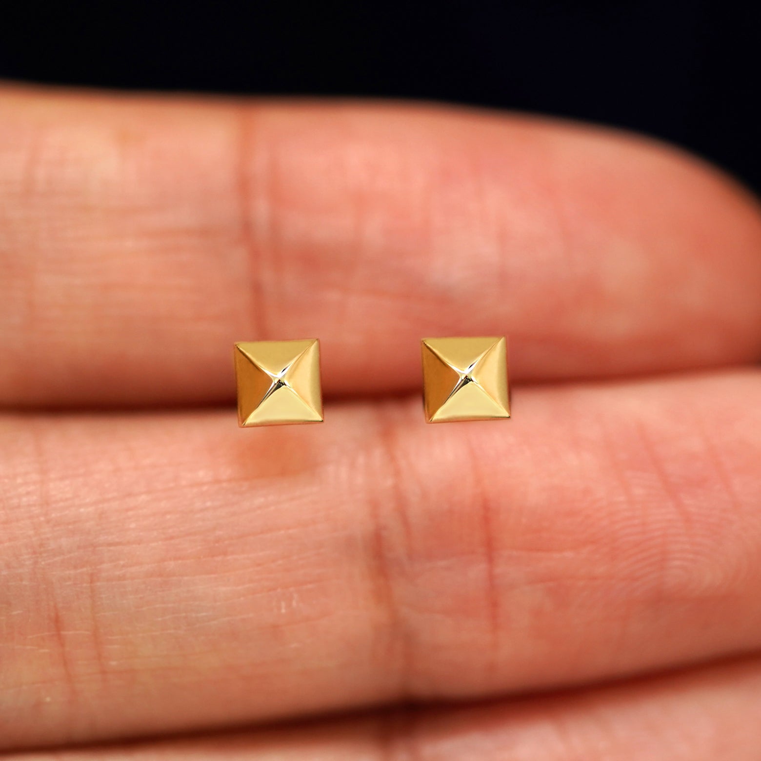 A pair of solid yellow gold Pyramid Earrings in between a model's fingers