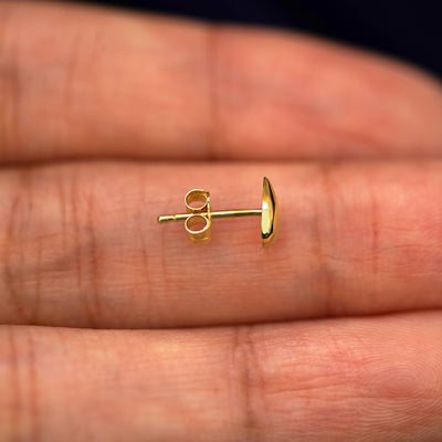 A 14k gold Teardrop Earring sitting sideways on a model's fingertips to show detail