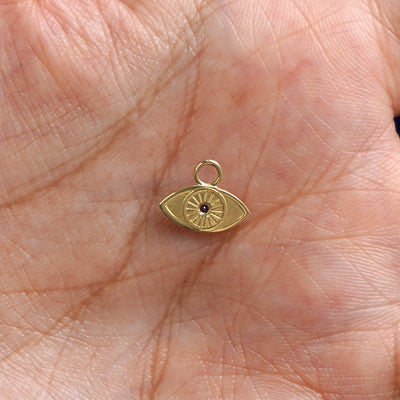 A 14k gold Evil Eye Charm for earring resting in a model's palm to show the back of the charm