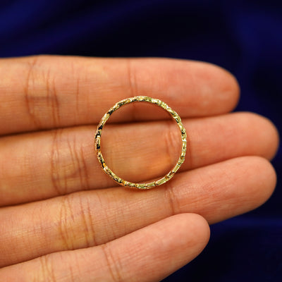 A yellow gold Double Leaves Band in a model's hand showing the thickness of the band