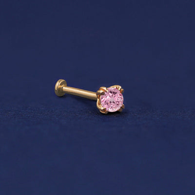 A 14 karat solid gold Pink Sapphire Flat Back Piercing on a dark blue background