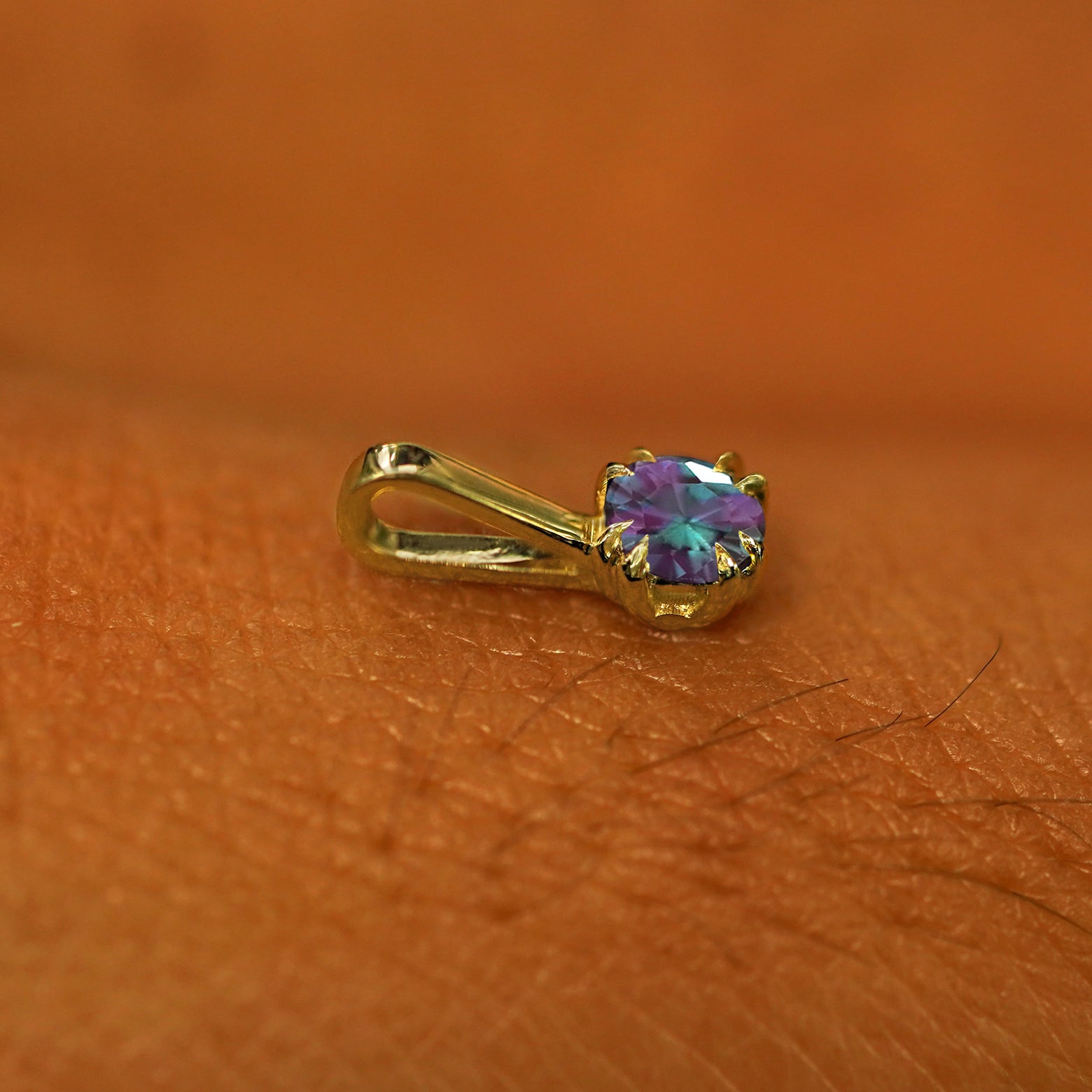 A 14k yellow gold Alexandrite Charm for chain resting on the back of a model's hand