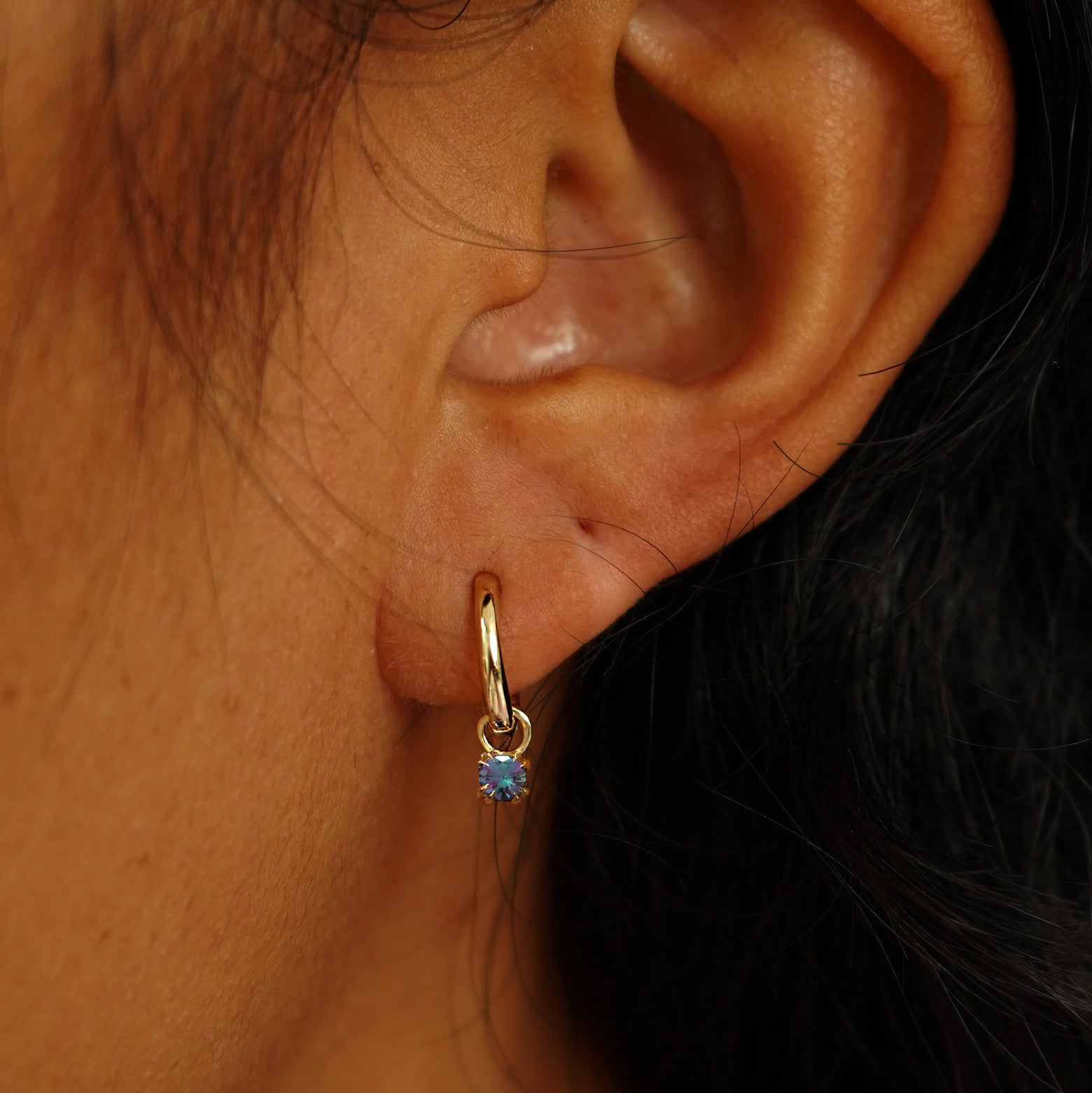 Close up view of a model's ear wearing a yellow gold Alexandrite Charm on a Curvy Huggie Hoop