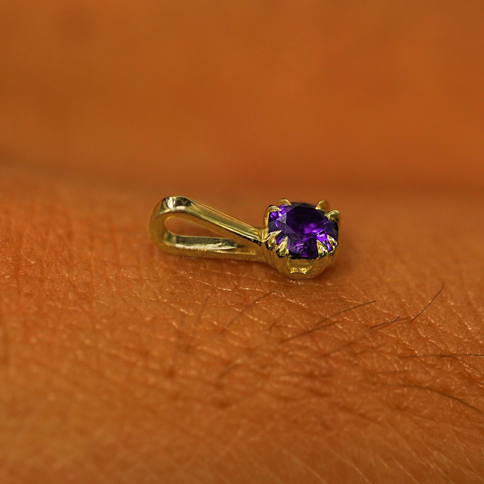 A 14k yellow gold Amethyst Charm for chain resting on the back of a model's hand