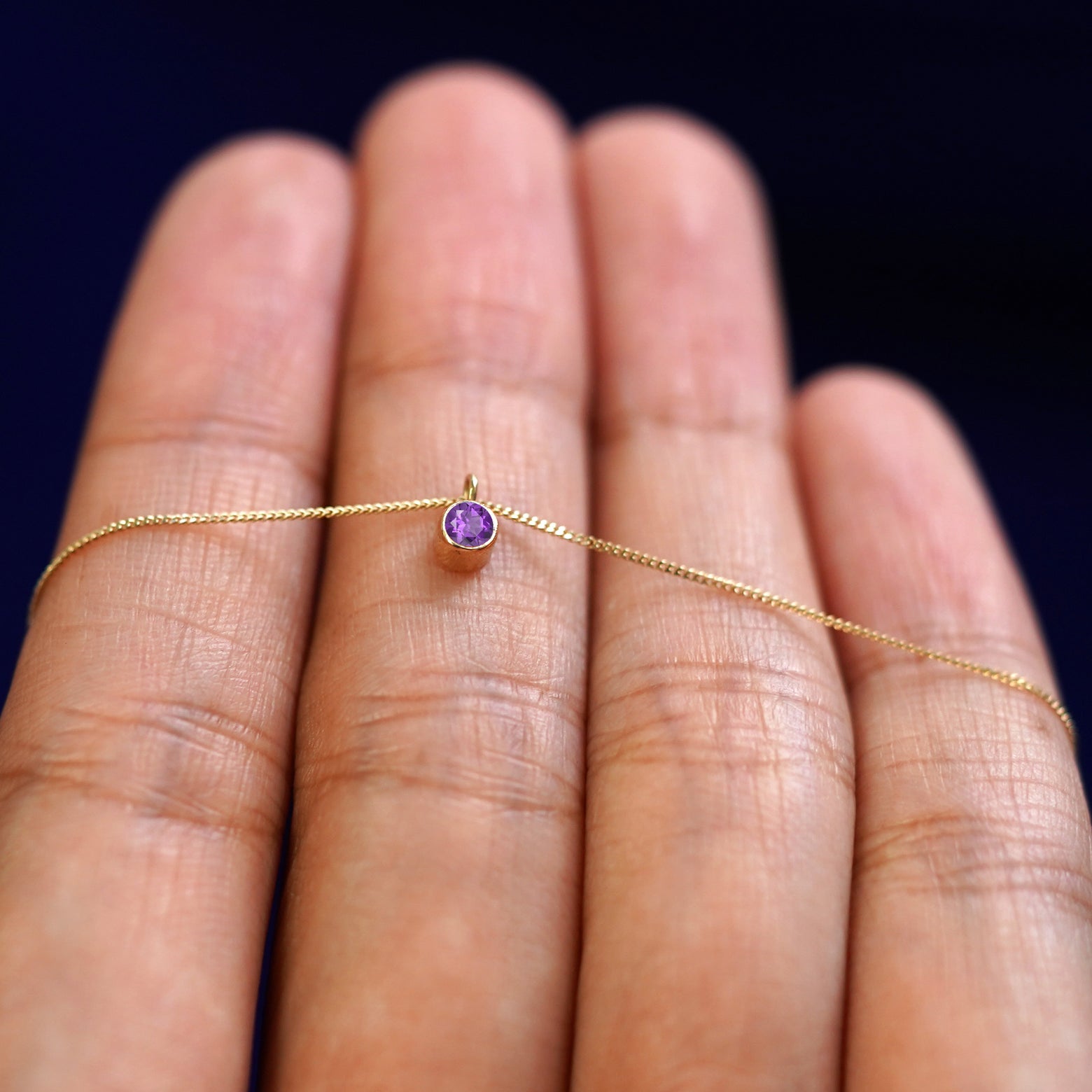 A 14k gold Amethyst Necklace draped over a model's fingers