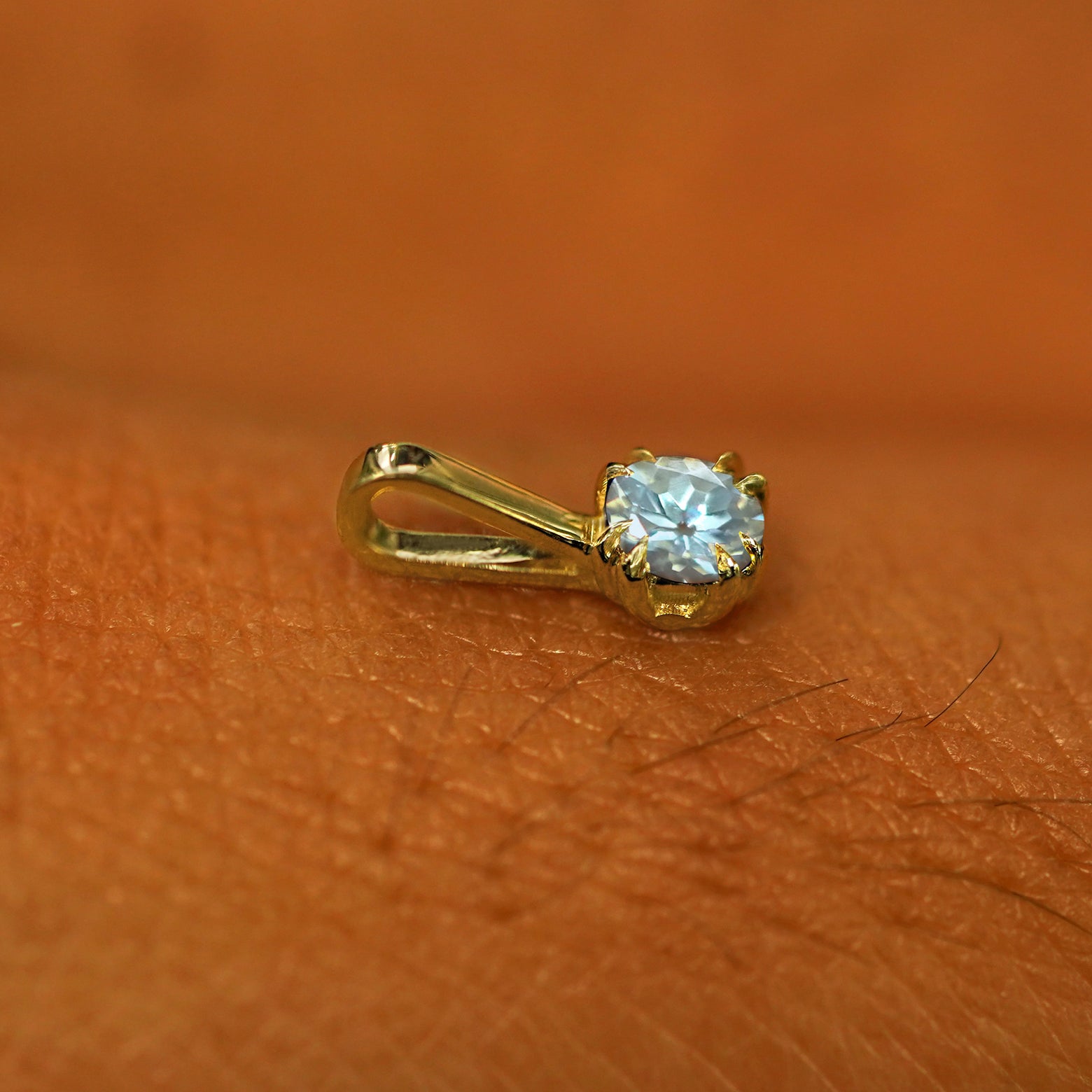 A 14k yellow gold Aquamarine Charm for chain resting on the back of a model's hand