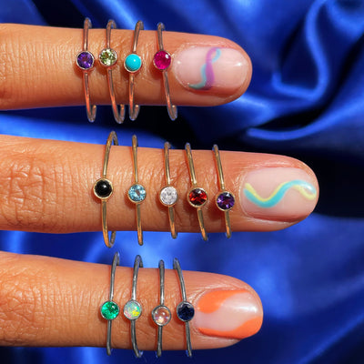 Three fingers with colorful wavy nail polish wearing various Automic Gold rings including a Peridot Ring