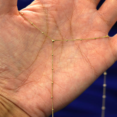 A yellow gold Beaded Essential Lariat Necklace stretched across a model's palm to show the details of the drop