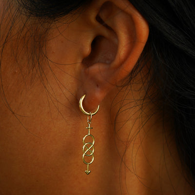 A model's ear wearing a yellow gold Bisexual Symbol Charm on a Curvy Huggie Hoop