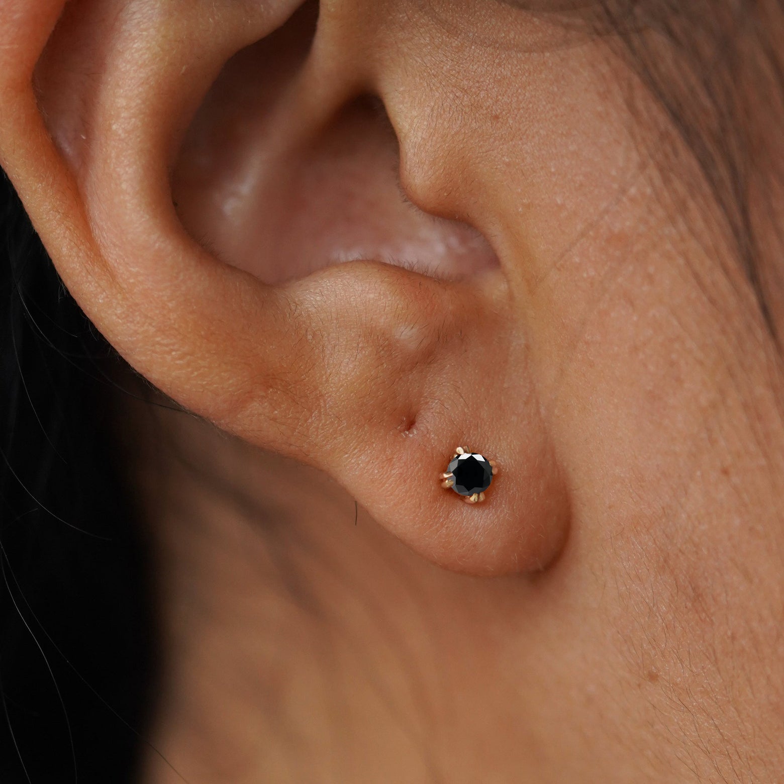 Close up view of a model's ear wearing a 14k yellow gold Black Diamond Earring