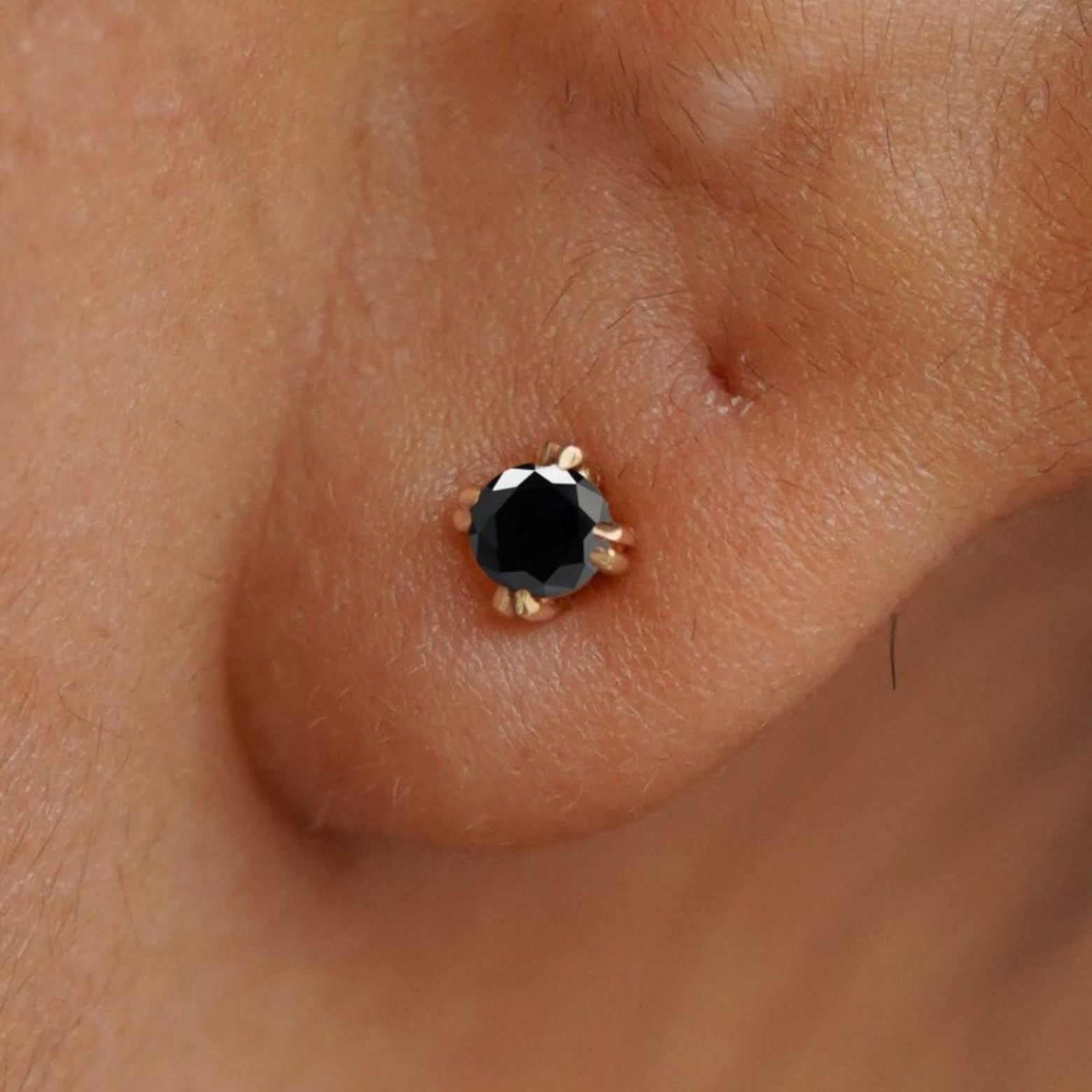 Close up view of a model's ear wearing a 14k yellow gold Black Diamond Stud Earring
