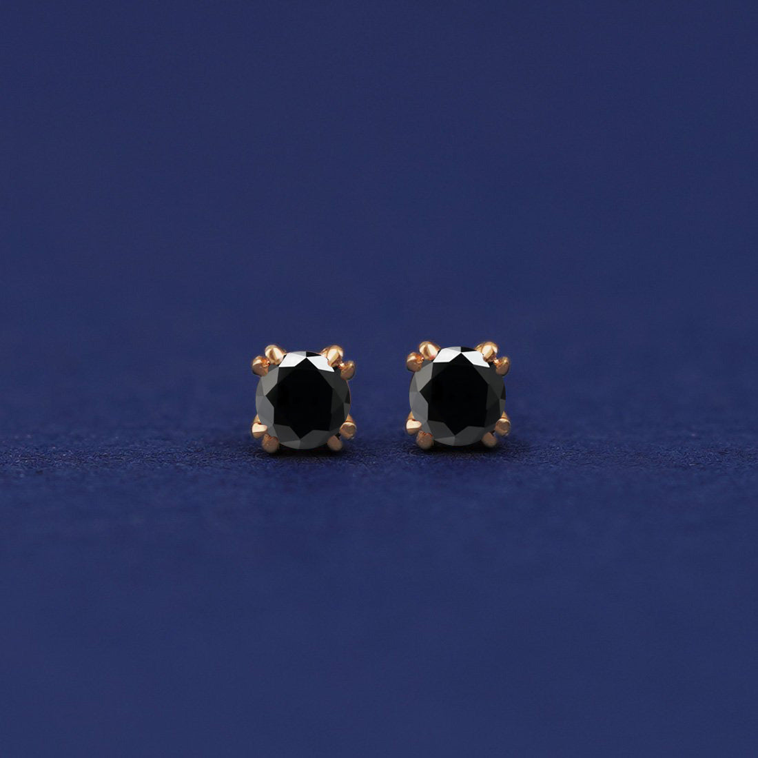 A pair of 14 karat gold studs earrings with 3 millimeter round 0.24ct Black Diamonds on a dark blue background