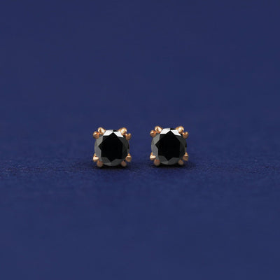 A pair of 14 karat gold studs earrings with 3 millimeter round 0.24ct Black Diamonds on a dark blue background