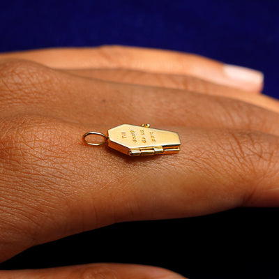 A closed 14k yellow gold Coffin Charm for chain balancing on the back of a model's finger