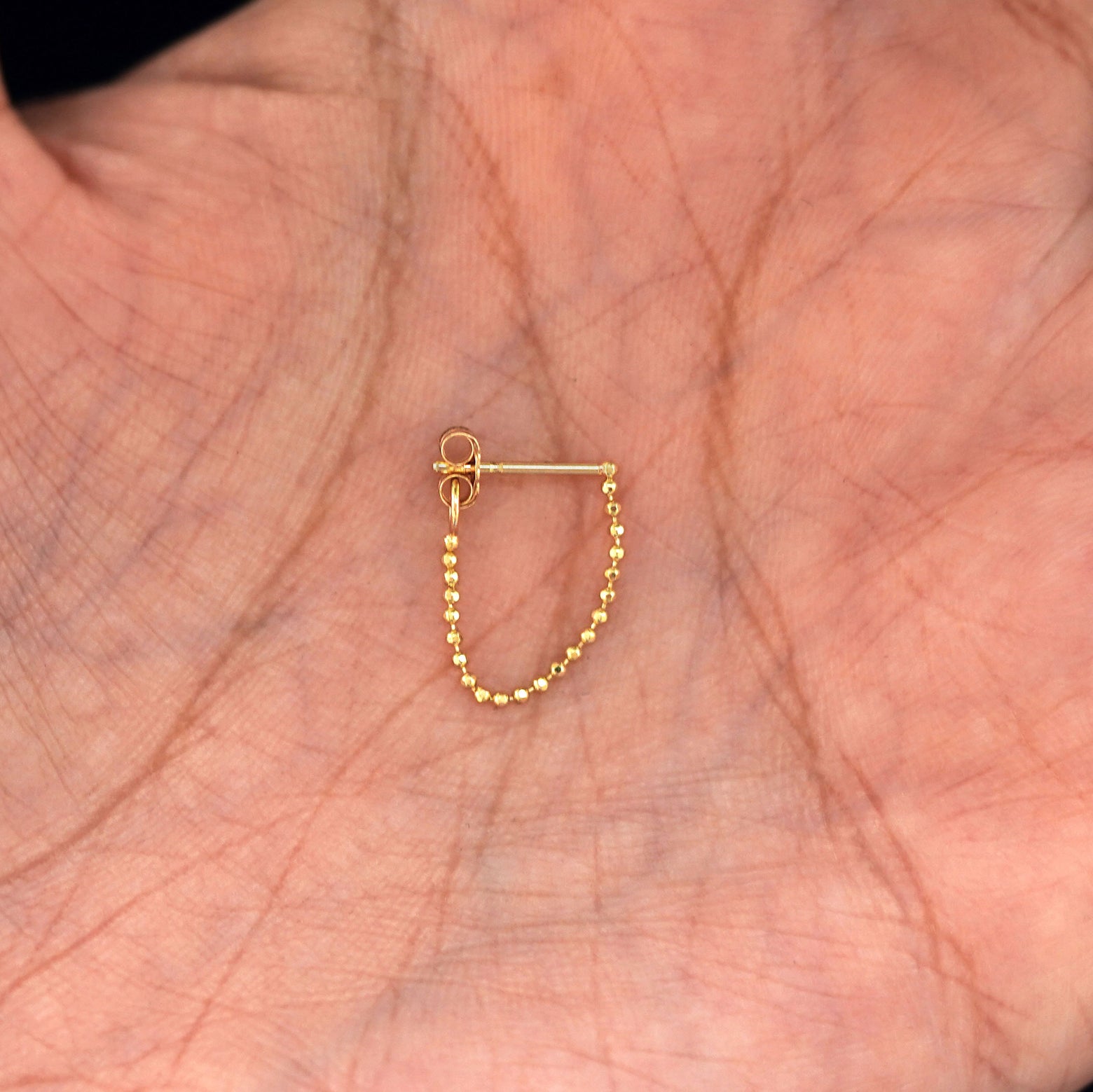 A solid yellow gold Chain Loop with the backing attached to post sitting in a model's hand