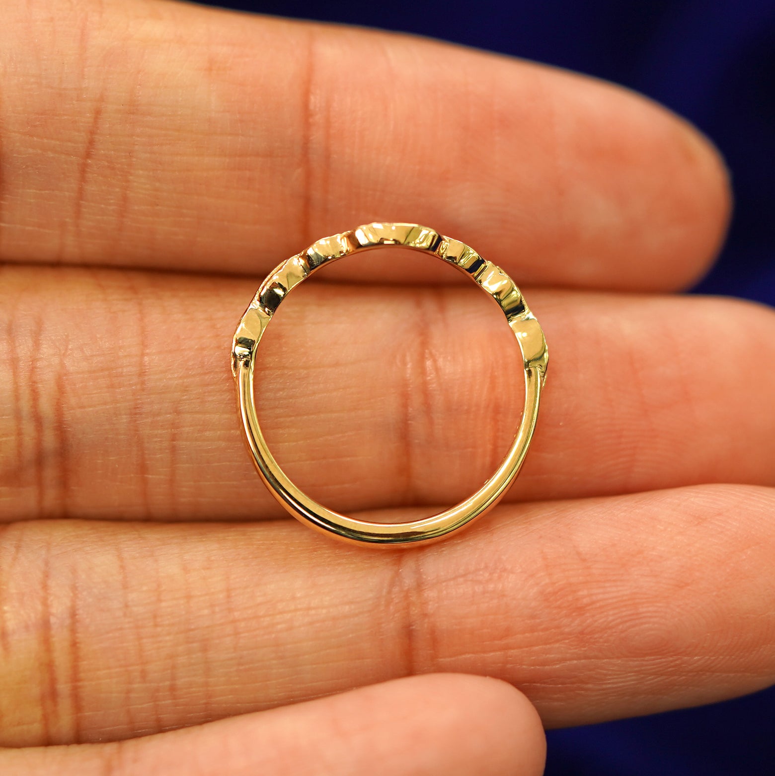 A yellow gold Chevron Leaves Band in a model's hand showing the thickness of the band