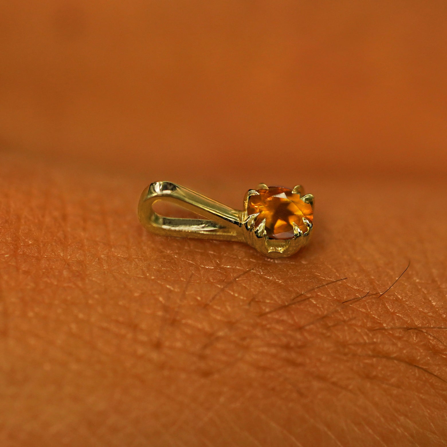 A 14k yellow gold Citrine Charm for chain resting on the back of a model's hand