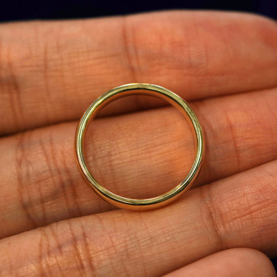 A yellow gold Mix Mirror Band in a model's hand showing the thickness of the band