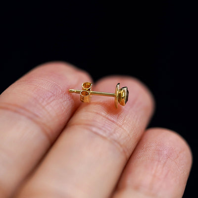 A 14k gold Coffee Cup Earring sitting sideways on a model's fingertips to show detail