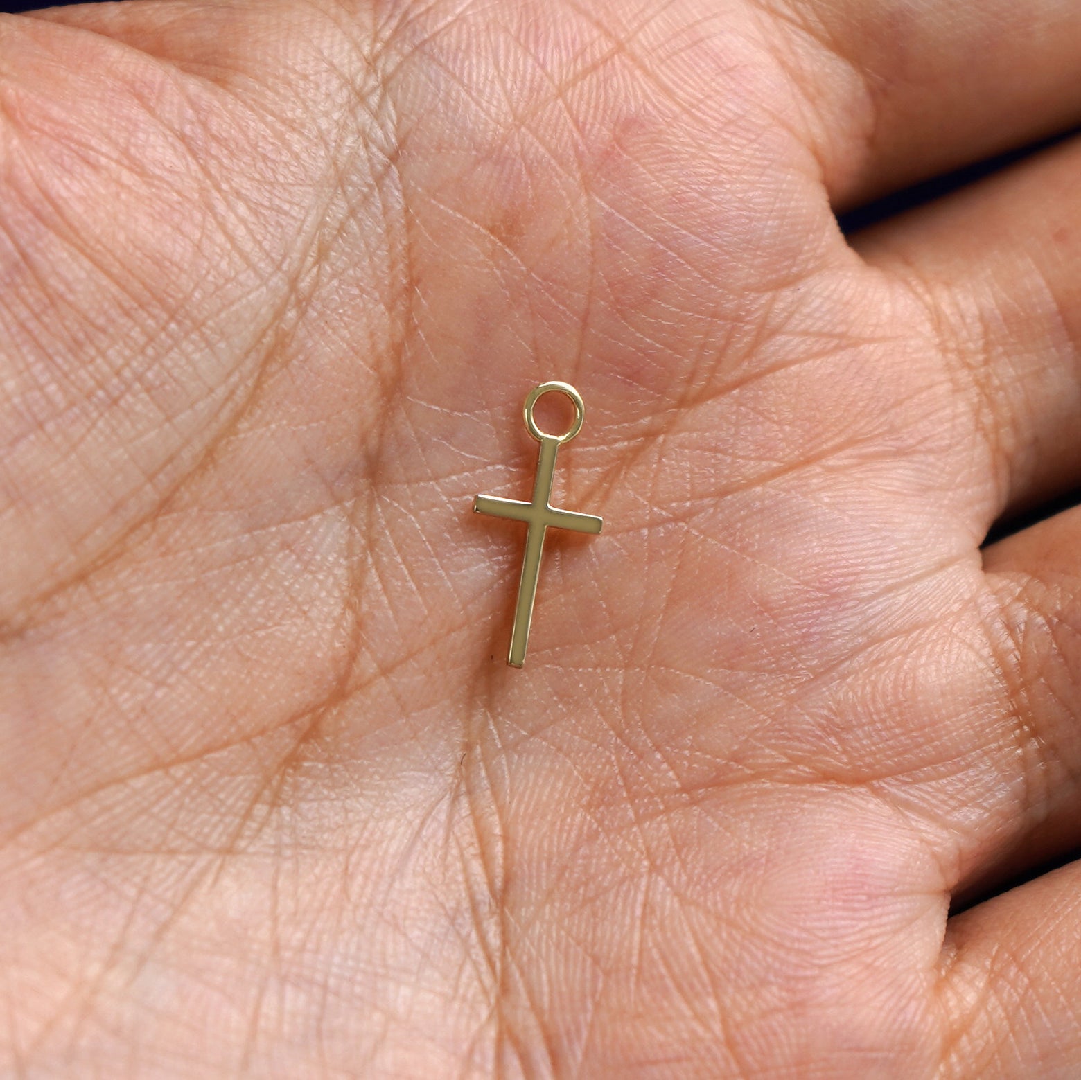 A solid gold Cross Charm for earring resting in a model's palm to show the underside of the charm