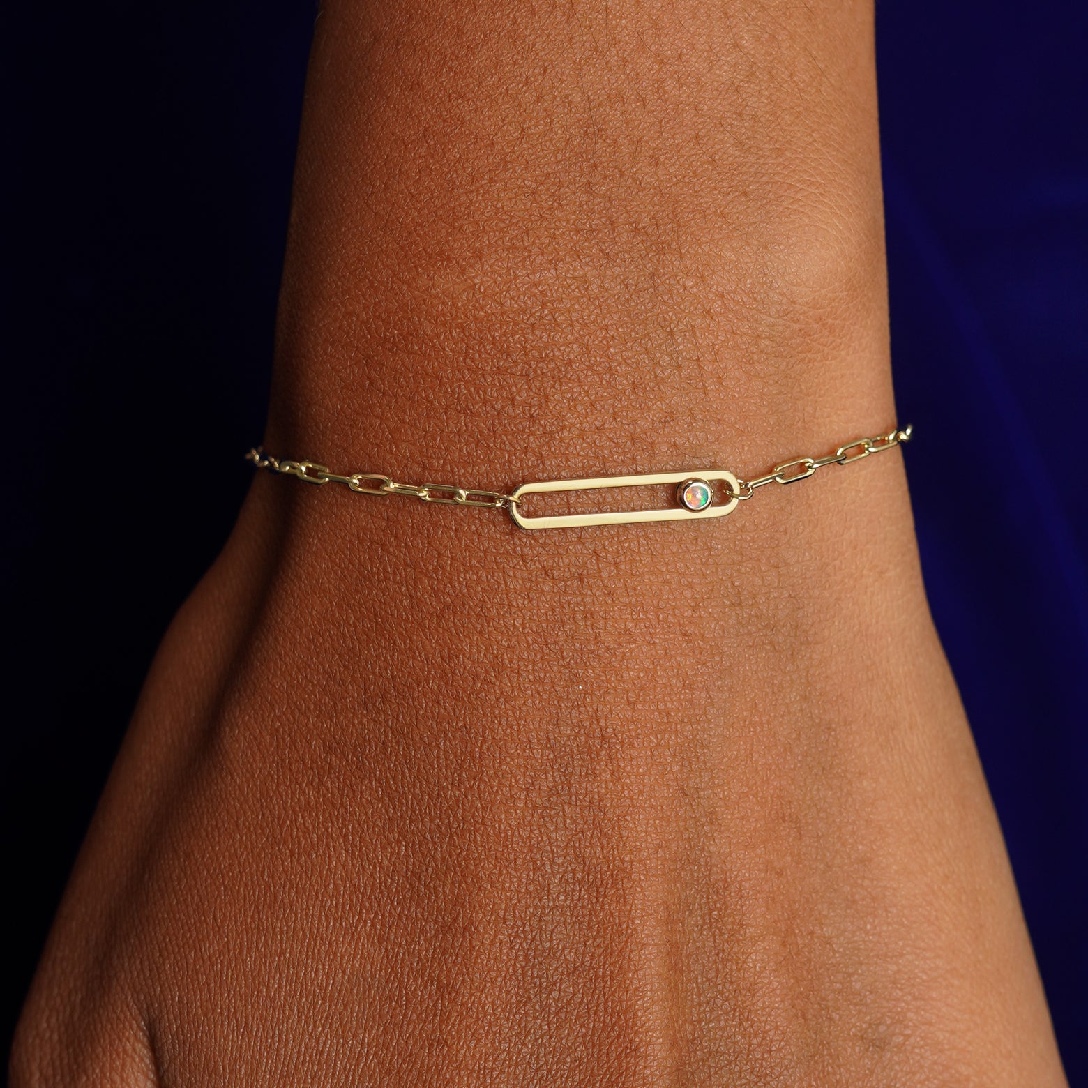 A model's wrist wearing a yellow gold Dancing Gemstone Bracelet with a single Opal