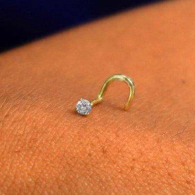 Close up view of a single 14k solid gold Diamond Nose Stud resting on the back on a model's hand