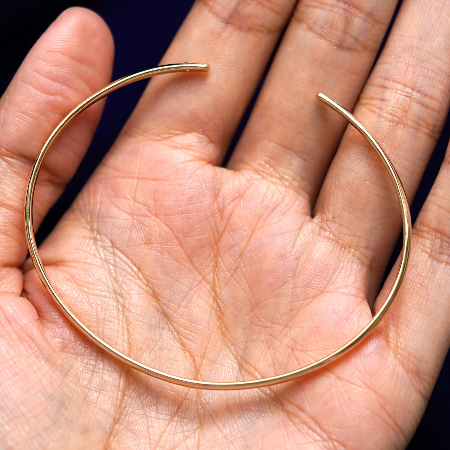 A yellow gold Diamond Open Bangle Bracelet sitting in a model's palm