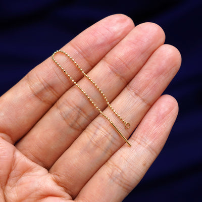 A solid 14k gold Extender held between a model's fingers to show the length of the diamond cut bead chain