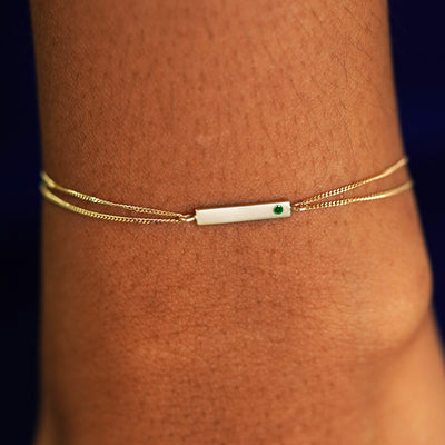 A model's wrist wearing a solid yellow gold emerald Gemstone Bar Bracelet