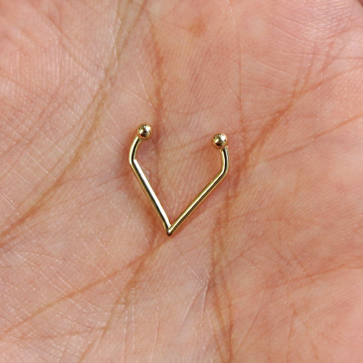 A model's hand holding a 14 karat yellow gold Non-Pierced Triangle Septum