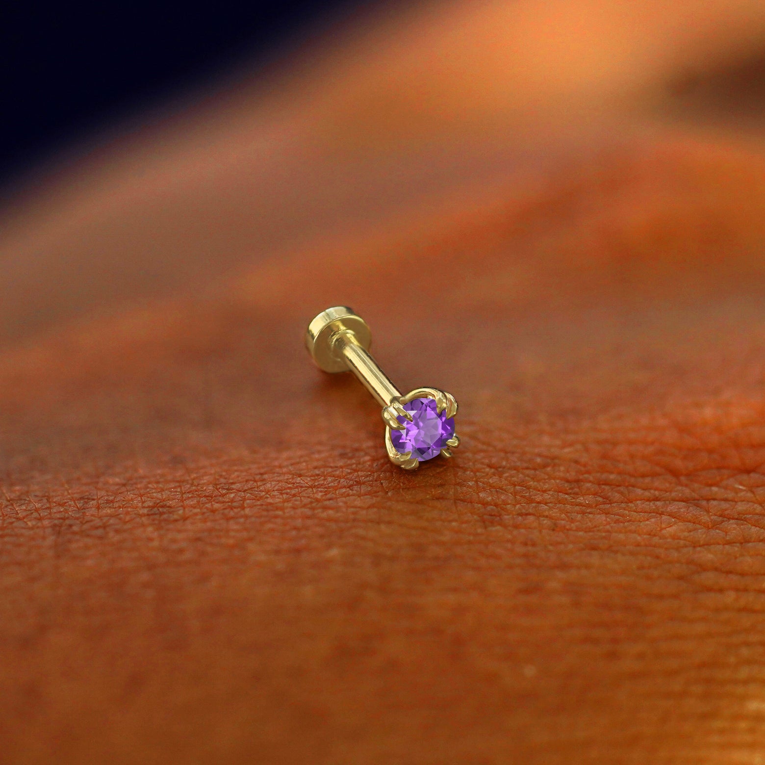 A solid 14k yellow gold Amethyst Flatback Piercing resting on the back of a model's hand