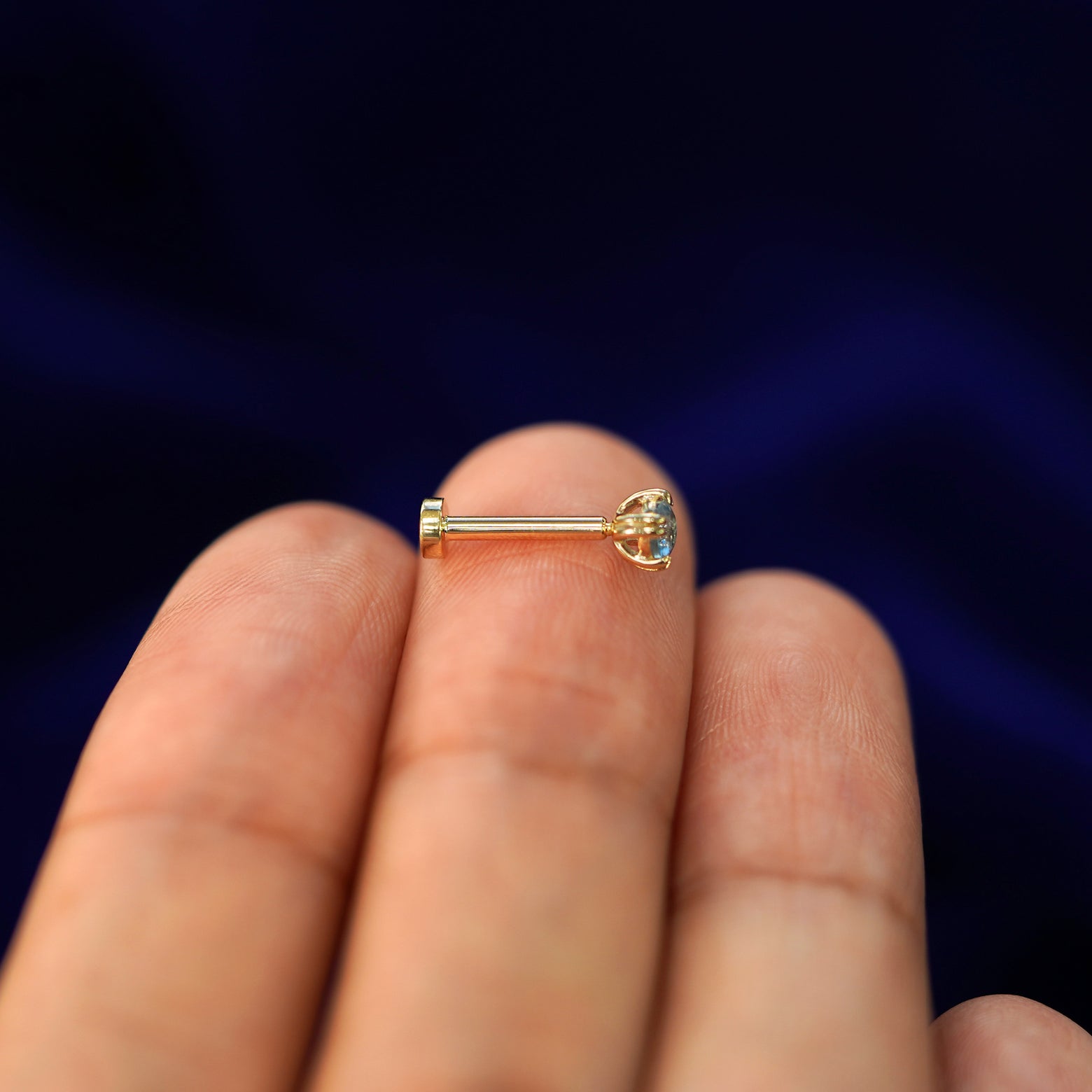 Side view of a yellow gold Aquamarine Flatback Piercing on a model's fingertips