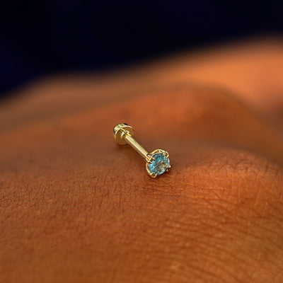 A solid 14k yellow gold Aquamarine Flatback Piercing resting on the back of a model's hand