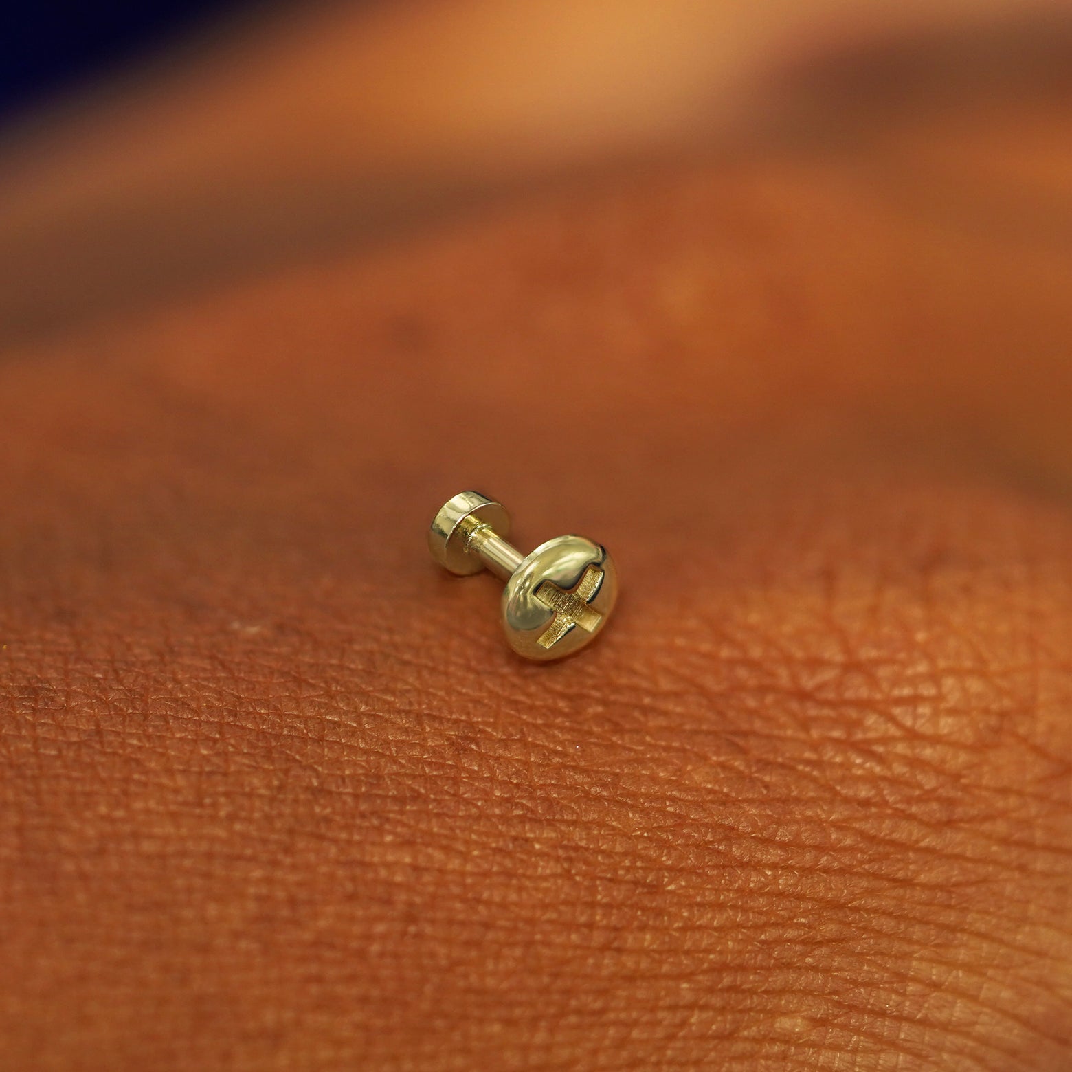 A solid 14k yellow gold Screw Flatback Piercing resting on the back of a model's hand