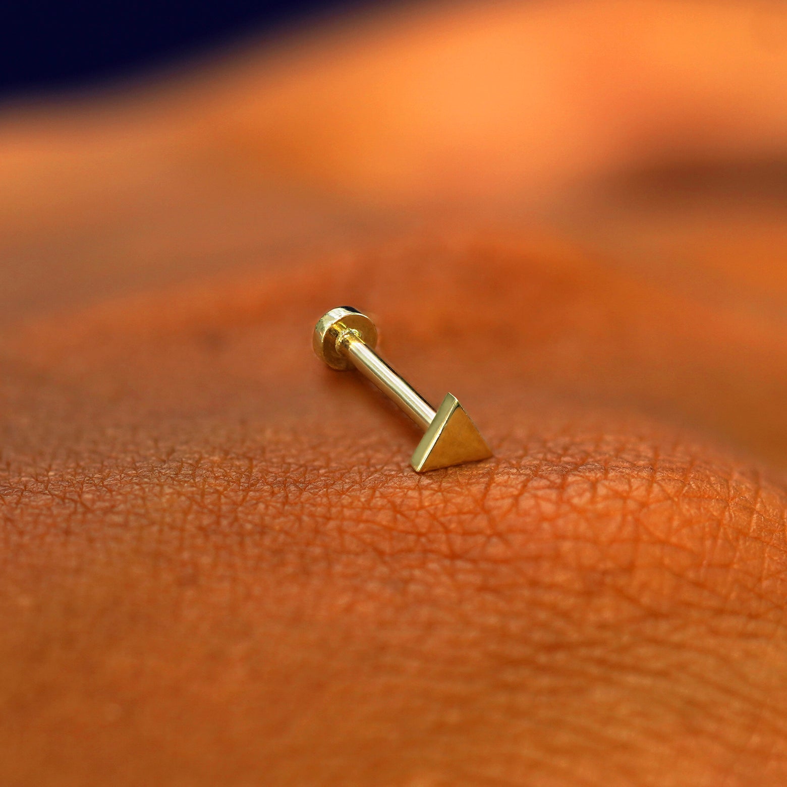 A solid 14k yellow gold Triangle Flatback Piercing resting on the back of a model's hand