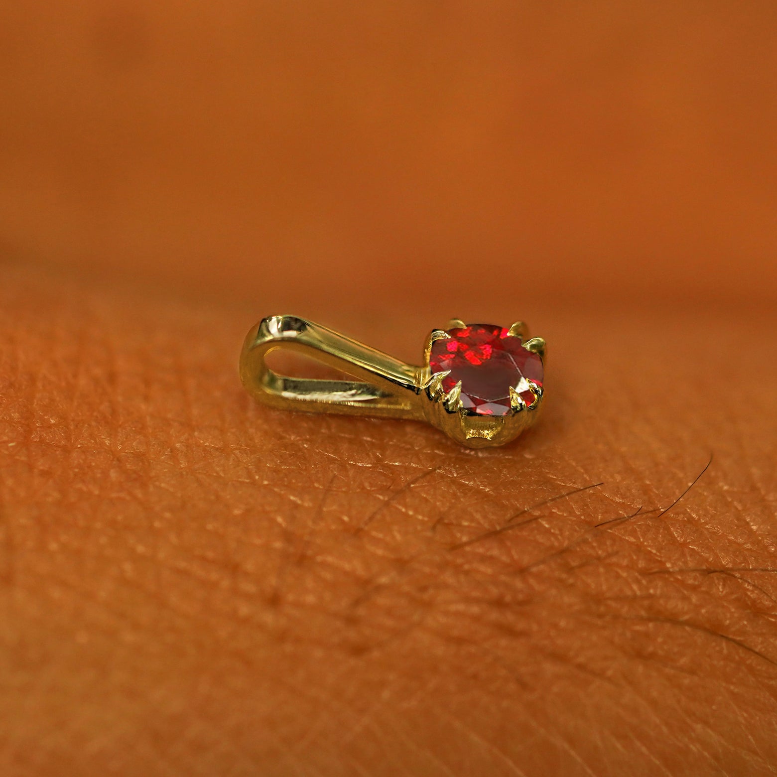 A 14k yellow gold Garnet Charm for chain resting on the back of a model's hand