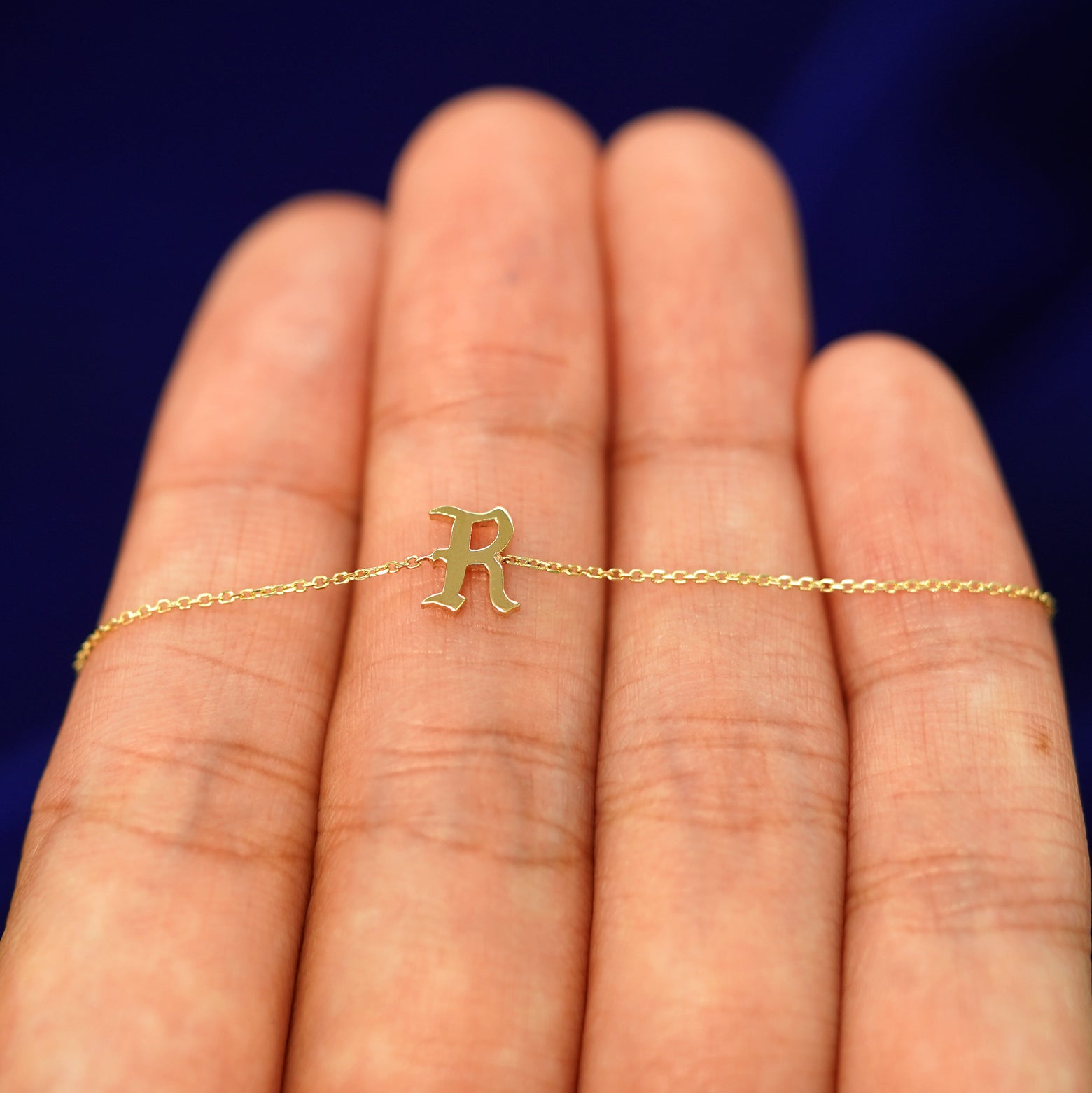 Close up view of a model's hand holding a yellow gold Initial Bracelet with the letter R