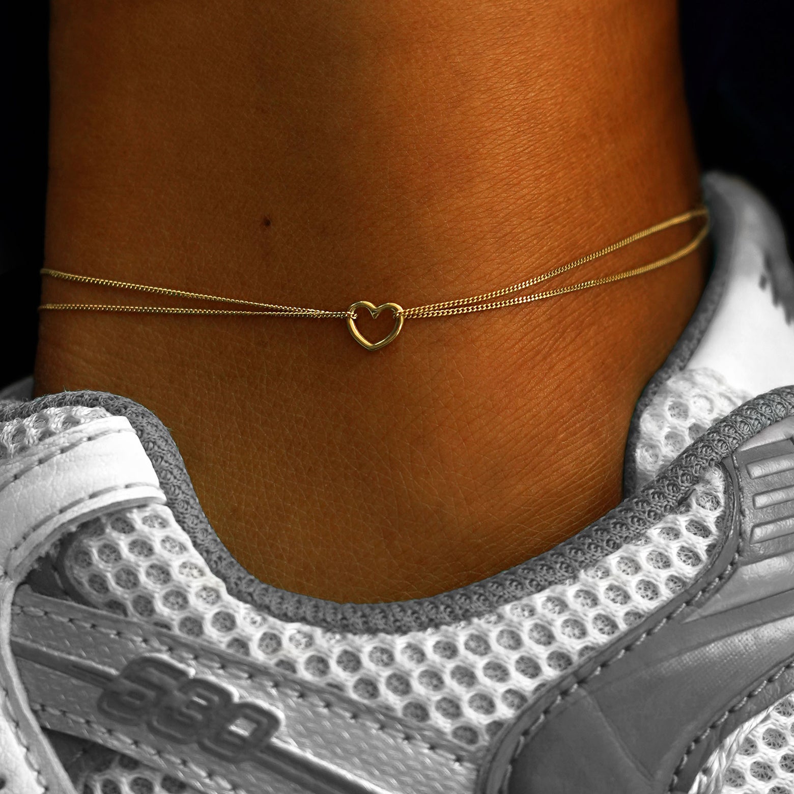 A model's ankle wearing a 14k yellow gold Heart Anklet